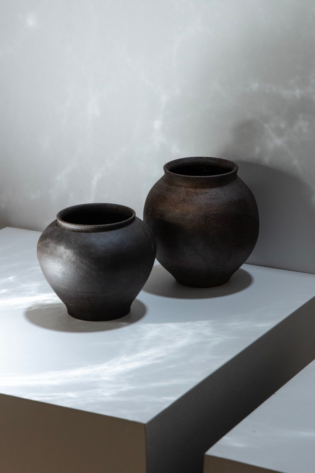 Two dark round vessels on a white plinth